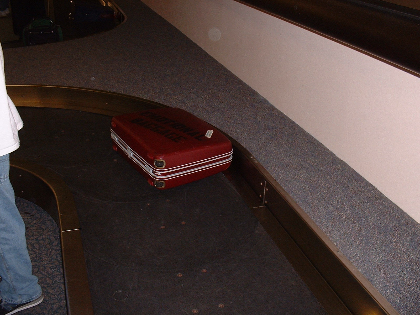 Image: Retro red suitcase with 'Emotional Baggage' stenciled on side on conveyor belt.