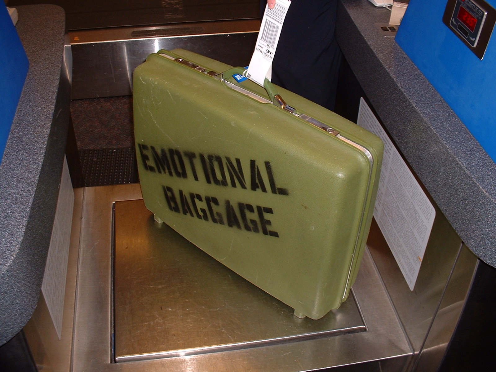 Image: Retro green suitcase with 'Emotional Baggage' stenciled on side being weighed.