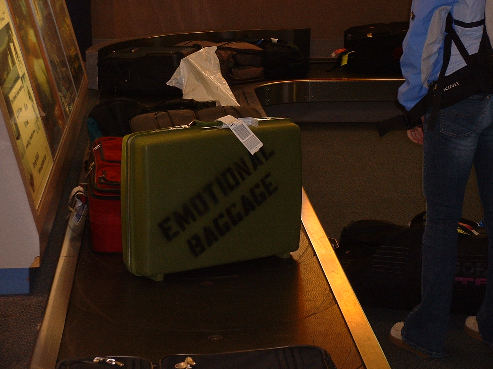 Image: Retro green suitcase with 'Emotional Baggage' stenciled on side on conveyor belt.