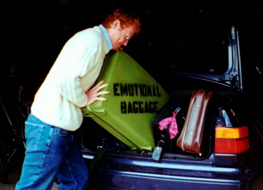 Image: Retro green suitcase with 'Emotional Baggage' stenciled on side with man putting it in trunk.